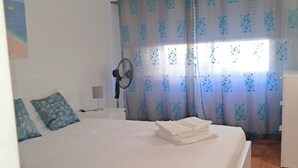 A bedroom with a bed, a fan, curtains, and a small desk.