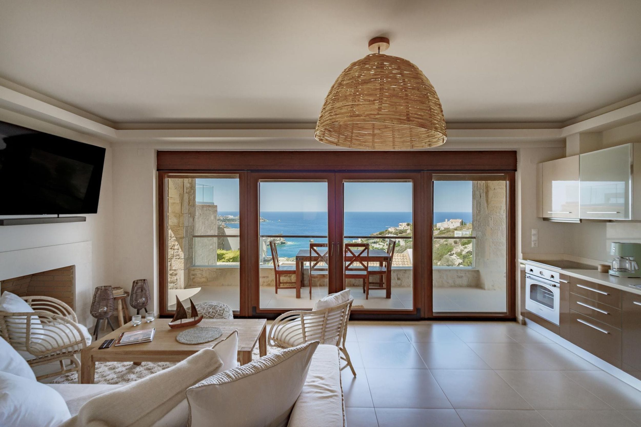 A spacious living room with a large TV, a dining area with a view of the sea, and a kitchen with modern appliances.