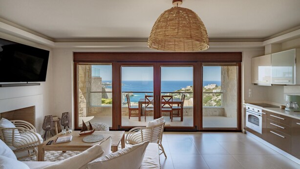 Un salón amplio con televisor grande, comedor con vista al mar y cocina equipada con electrodomésticos modernos.