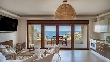 A spacious living room with a large TV, a dining area with a view of the sea, and a kitchen with modern appliances.