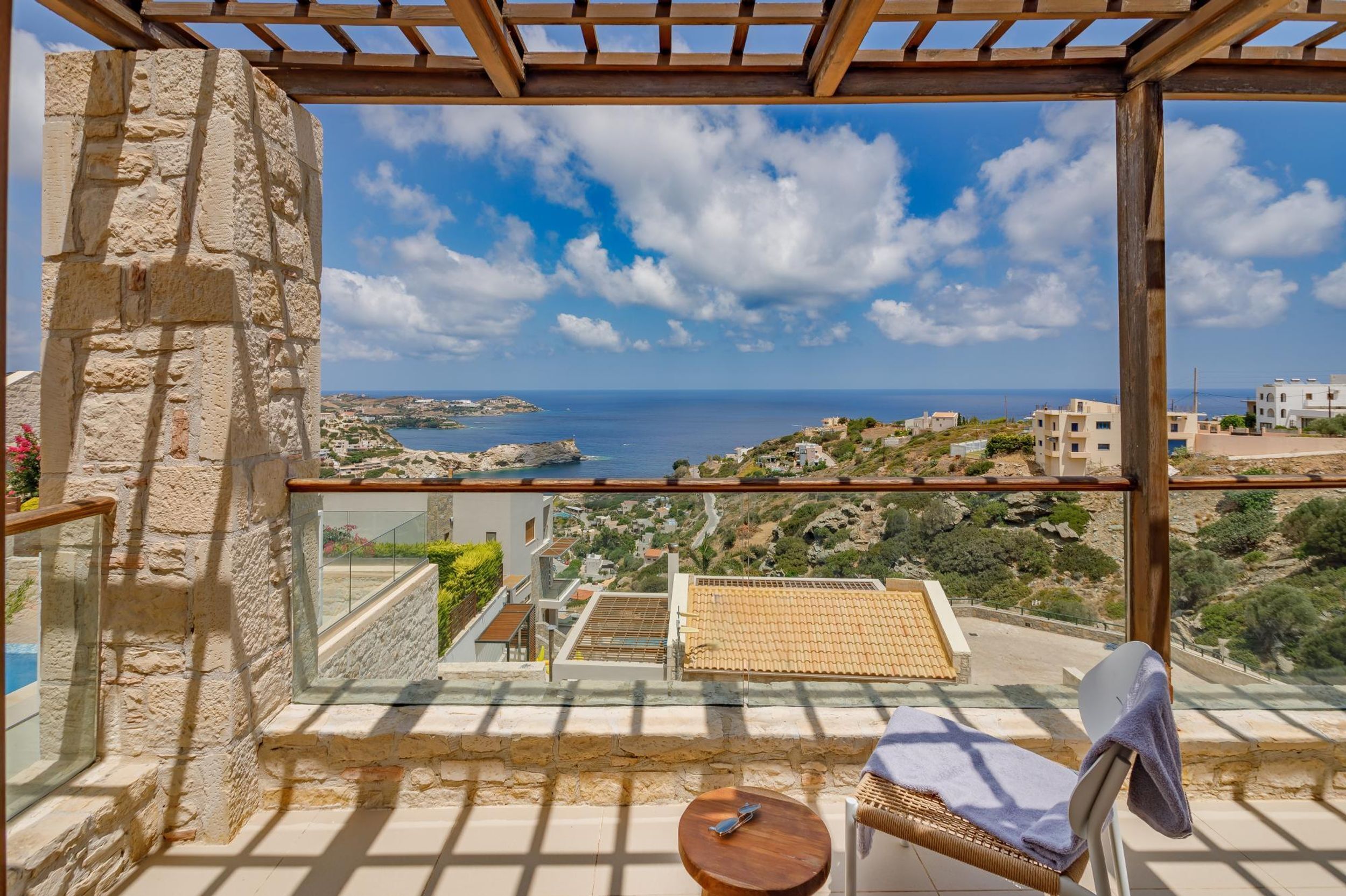 A balcony with a stone wall, a view of the sea, and a small table with a chair.