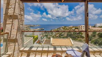 A balcony with a stone wall, a view of the sea, and a small table with a chair.