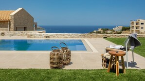 Una piscina con dos faroles de mimbre, una silla con una toalla y vista al mar.