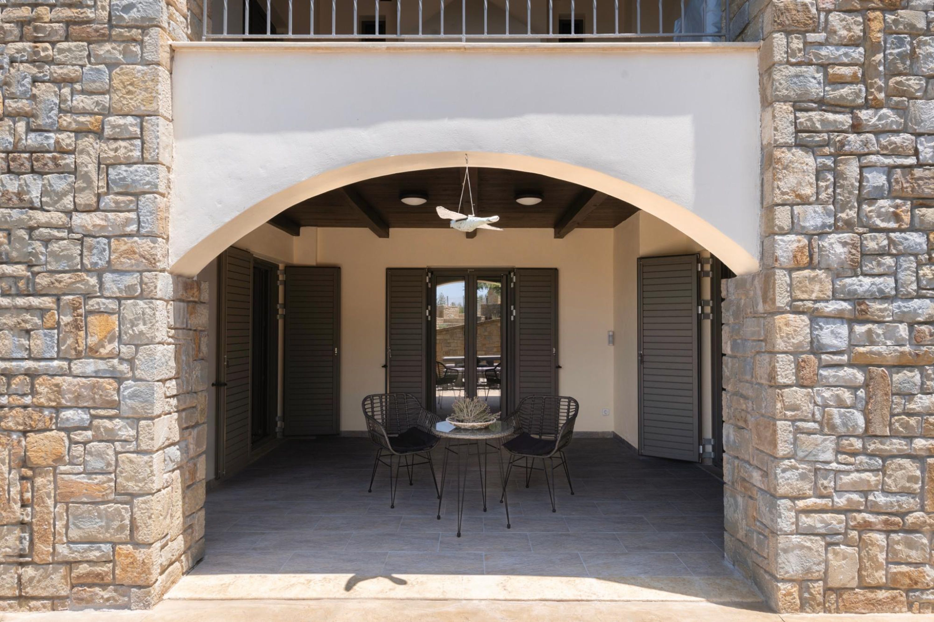 An outdoor patio with stone walls, a covered seating area, and a ceiling fan.