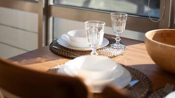 Una mesa de comedor con platos, vasos y un bol, frente a una ventana con vistas a la ciudad.