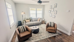 A living room with a sofa, two armchairs, a coffee table, a floor lamp, and a ceiling fan.