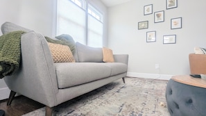 A living room with a grey sofa, a patterned rug, and a wall with framed artwork. - Cozy 3 BdRm Cape Cottage in Green Park, RVA - 10 minutes 2 Downtown  (Richmond)