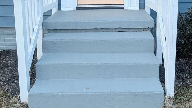 A house with a beige front door, white railings, and a blue exterior.