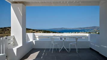 A balcony with a table and chairs, overlooking a coastal landscape with a clear sky.