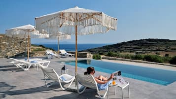 A poolside area with lounge chairs and umbrellas, overlooking a scenic view.