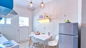 Una cocina moderna con una mesa blanca, dos sillas blancas, un refrigerador de acero inoxidable y lámparas colgantes.