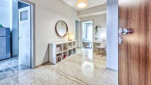 Un interior moderno con suelo de mármol, una estantería blanca, un espejo redondo y una zona de comedor con mesa y sillas.