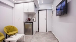 A compact kitchen with white cabinets, a built-in oven, and a small refrigerator. There is a white table with two chairs, and a television mounted on the wall. - Exclusive New Modern Apartment at Syntagma Square (Athina)