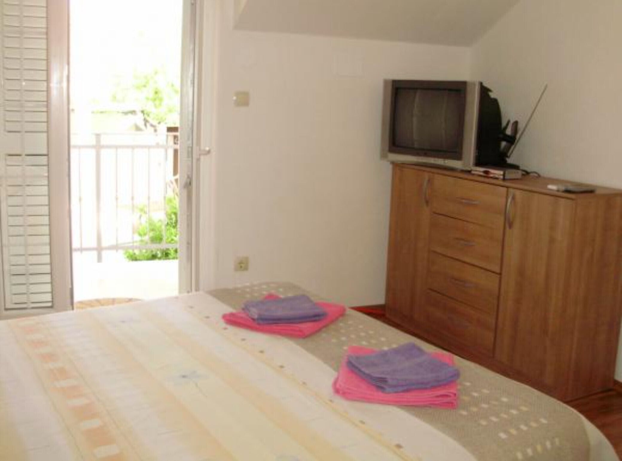 Ein Schlafzimmer mit einem Bett, einem Holzschrank, einem Fernseher darauf und einer Tür zu einem Außenbereich.