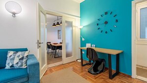 Ein Zimmer mit einer türkisfarbenen Akzentwand, Holzboden, einem blauen Sofa, einem Schreibtisch mit Stuhl und einer Wanduhr.