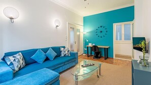 Ein modernes Wohnzimmer mit einem blauen Sofa, einem Glastisch und einer türkisfarbenen Wand.