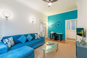 A modern living room with a blue sofa, glass coffee table, and a teal accent wall. - Acropolis Stylish 2BR Apartment - Center of Athens (Athina)