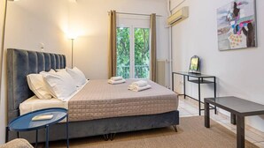 Ein Hotelzimmer mit Bett, Nachttisch, Lampe und Blick auf Grünfläche.