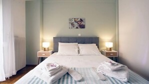 Hotellihuone, jossa on sänky, kaksi yöpöytää valaisimineen, patteri ja seinälle ripustettu taideteos.