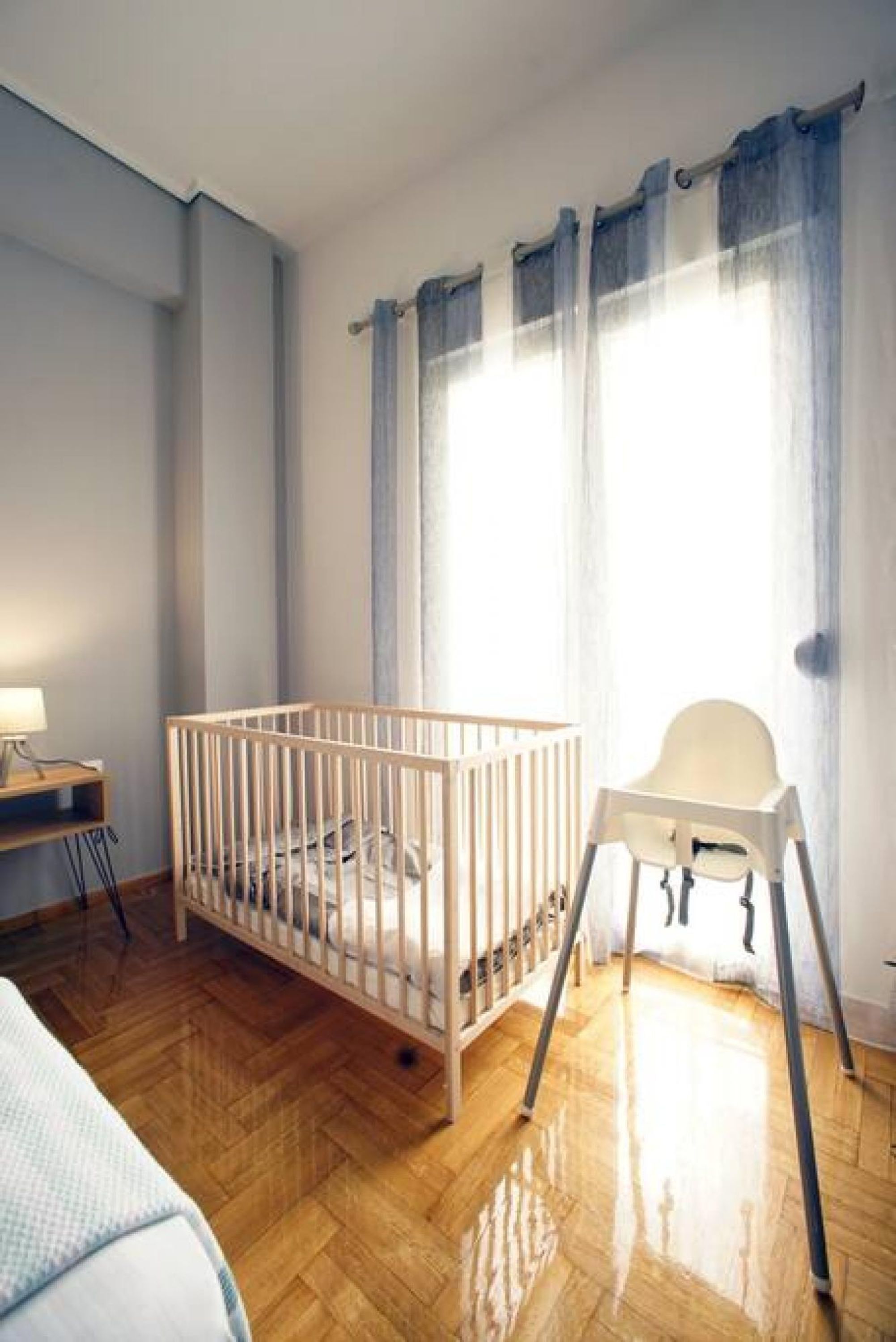 Una habitación para bebés con una cuna de madera, una trona y un escritorio con lámpara.