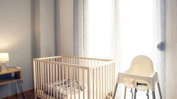 Una habitación para bebés con una cuna de madera, una trona y un escritorio con lámpara.