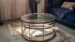 A round glass coffee table with a metal frame, a vase with flowers, and a blue sofa with patterned cushions.