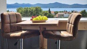 A balcony with two leather chairs and a wooden table, a bowl of fruit, and a scenic view of mountains and a lake.
