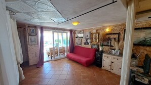 Una sala de estar con sofá rojo, piso de baldosas y chimenea.