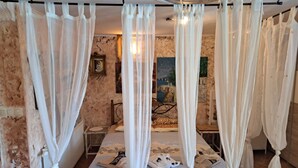 Un dormitorio con una cama, cortinas blancas, un cuadro en la pared y una mesita.