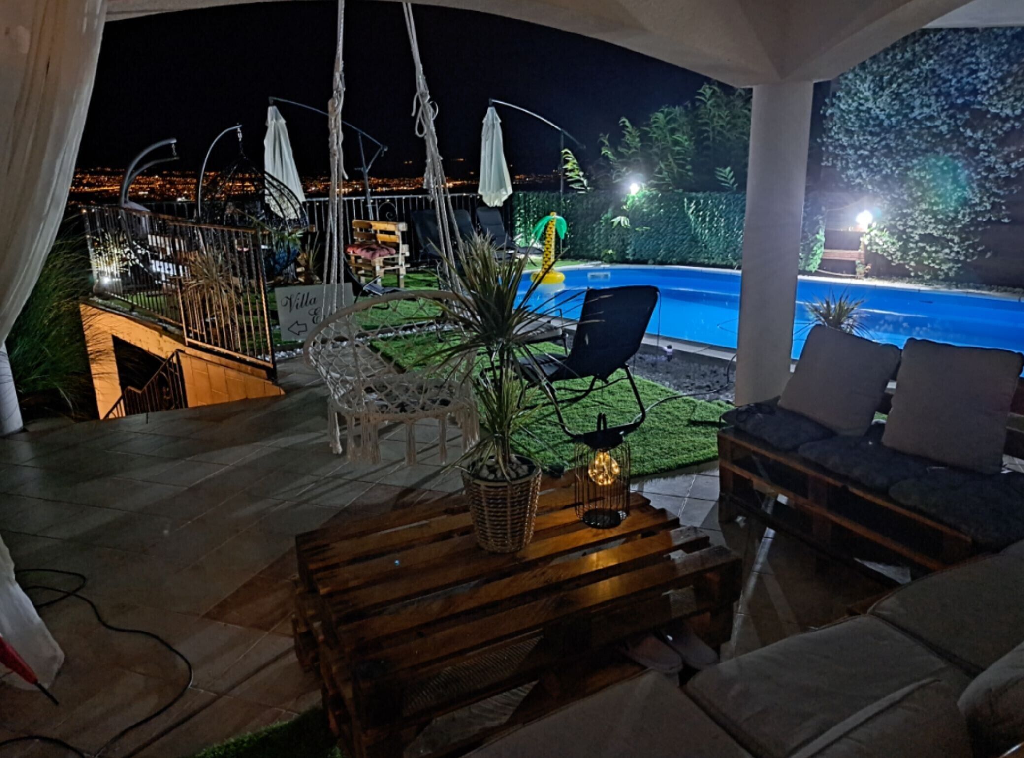 A patio area with outdoor seating, a pool, and a view of the city at night.