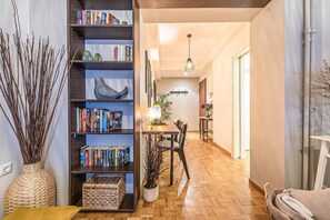 A modern living room with a wooden floor, a bookshelf, a dining area with a table and chairs, and a decorative vase with branches. - Bohemian Chic 1BR Apartment in the Heart of Athens (Athina)