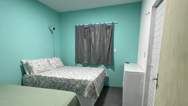 Een kleine, eenpersoonskamer met een bed, een klein tafeltje, een raam met gordijnen en een deur.