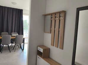 Een moderne kamer met een eettafel, stoelen, een klein houten kastje en een spiegel met haken.