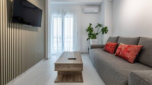 Uma sala de estar moderna com uma televisão de tela plana na parede, um sofá cinza com almofadas vermelhas, uma mesa de centro de madeira e um vaso com planta.
