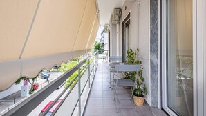 Uma varanda estreita com grade de metal, uma mesa pequena e plantas em vasos.
