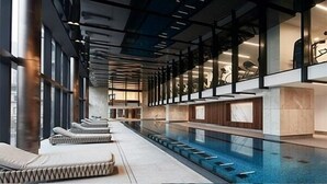 Zona de piscina interior moderna amb gandules, paret de vidre i sostre amb bigues a la vista.