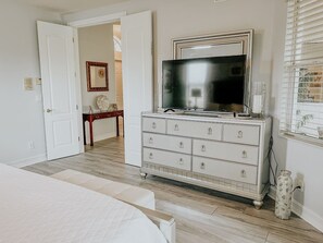 Une chambre à coucher comprenant un lit, une commode avec des tiroirs, un téléviseur et une porte donnant sur une autre pièce.