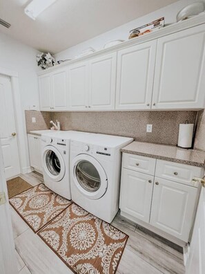 A compact laundry area with two washing machines, a countertop, and cabinets.