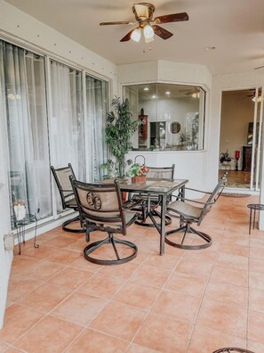 Zona pranzo con tavolo e sedie, una ventola a soffitto e un'ampia finestra con tende.