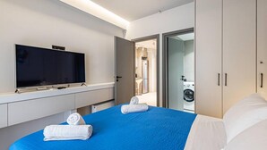 Moderni hotellihuone, jossa on suuri sänky, taulutelevisio, pesukone ja kylpyhuone, joka näkyy avoimesta ovesta.