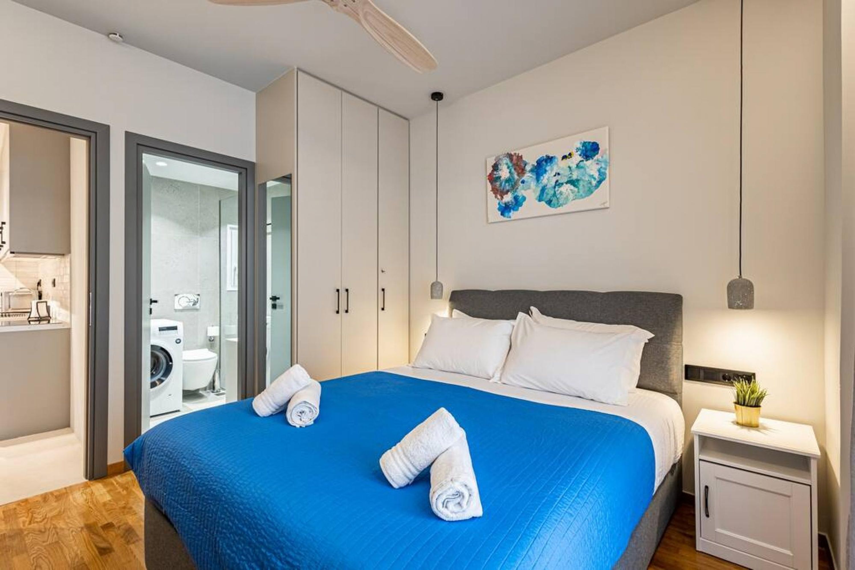 Une chambre d’hôtel moderne dotée d’un grand lit, d’une salle de bain avec machine à laver et d’une porte vitrée donnant sur une autre pièce.