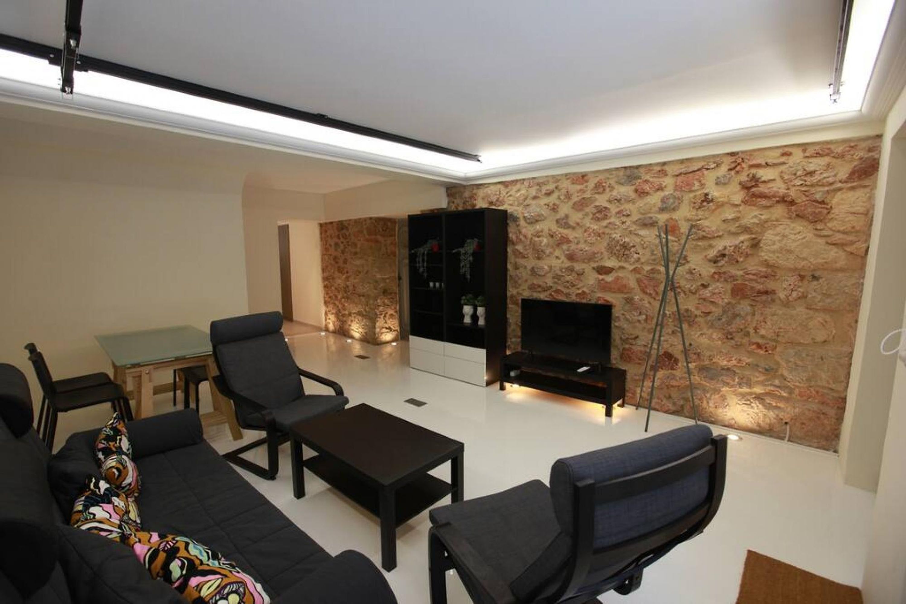 A modern living room with a sofa, chairs, a coffee table, a TV, and a stone wall.