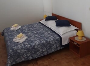 A neatly made bed with floral bedding, two pillows, and folded towels. There is a bedside table with a lamp and a small rug. - Apartment Almira - One bedroom apartment with sea view (Omis)