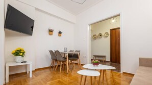 A modern living room with a flat-screen TV, a dining area with a table and chairs, and a sofa. - Roubnb Acropolis Museum 1BD Apt (Athina)