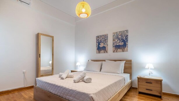 A bedroom with a wooden bed, a nightstand with a lamp, and two wall art pieces. - Roubnb Acropolis Museum 1BD Apt (Athina)