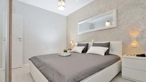 Un dormitorio moderno con una cama grande, mesitas de noche, un espejo y una lámpara de techo.