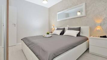 A modern bedroom with a large bed, bedside tables, a mirror, and a ceiling light.