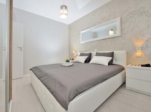 Une chambre moderne avec un grand lit, des tables de chevet, un miroir et un luminaire au plafond.