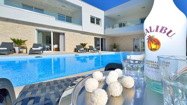 Un espace moderne au bord de la piscine, avec une bouteille de rhum Malibu, un plateau de bouchées à la noix de coco et des chaises longues.