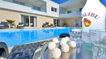 A modern poolside area with a bottle of Malibu rum, a tray with coconut balls, and lounge chairs.